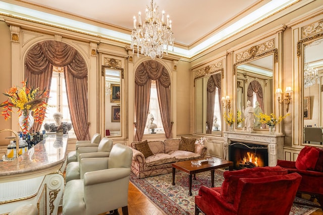 living area featuring crown molding, a fireplace, a decorative wall, and an inviting chandelier