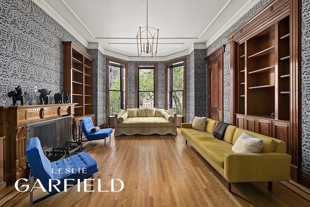 living area with an inviting chandelier, hardwood / wood-style flooring, ornamental molding, and built in shelves