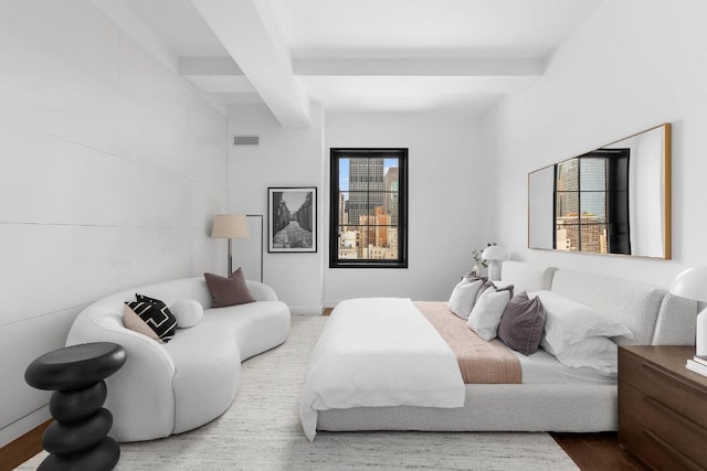 bedroom with multiple windows, beam ceiling, and hardwood / wood-style floors