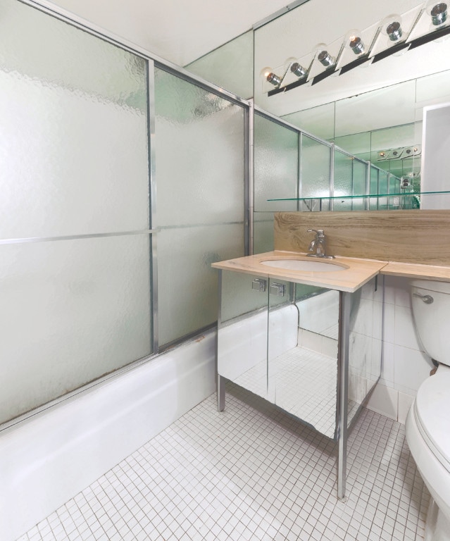 full bathroom featuring bath / shower combo with glass door, sink, tile patterned floors, and toilet