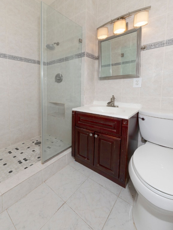 bathroom with tile walls, vanity, a tile shower, decorative backsplash, and toilet