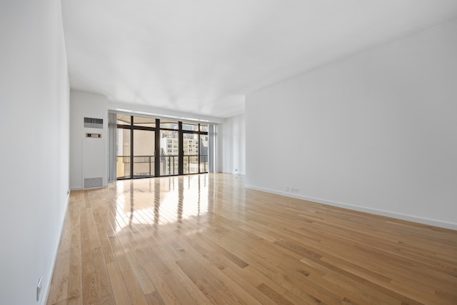 unfurnished living room with expansive windows, light wood finished floors, visible vents, and baseboards