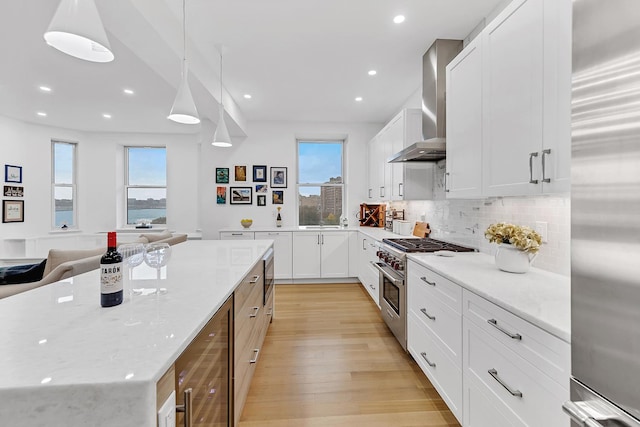 kitchen featuring high quality appliances, wall chimney range hood, light wood-style flooring, plenty of natural light, and recessed lighting