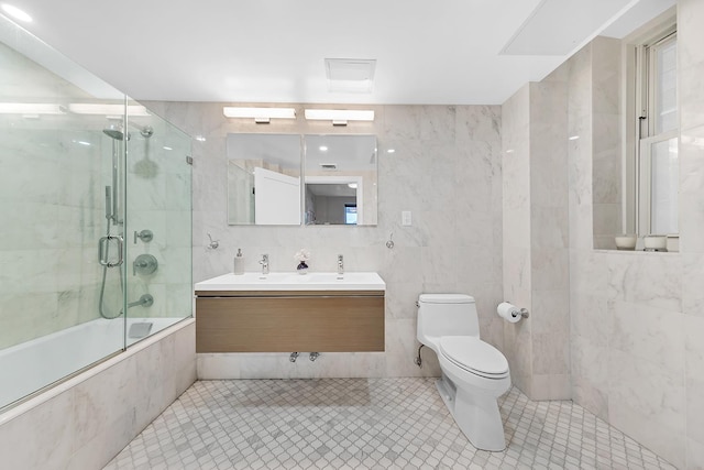 bathroom featuring double vanity, toilet, tile walls, tile patterned flooring, and tiled shower / bath