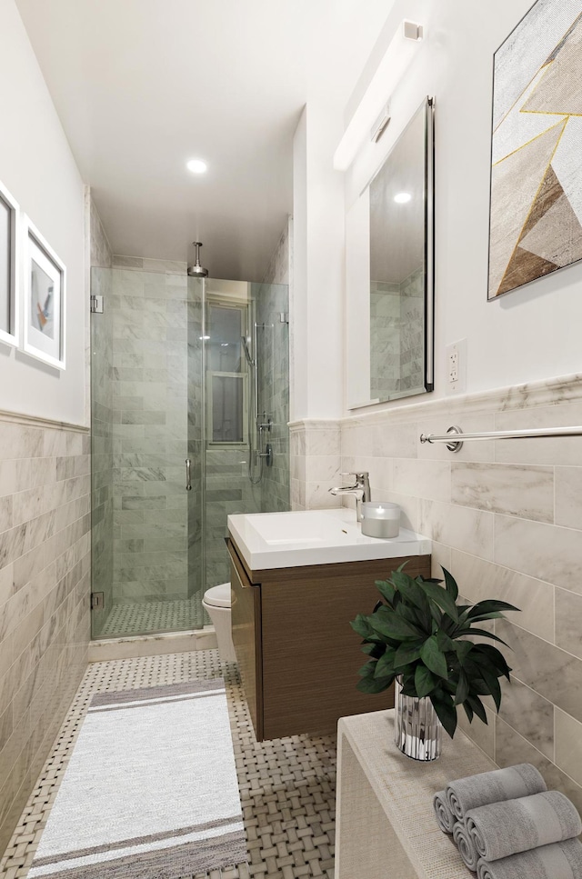 bathroom with a shower stall, wainscoting, vanity, tile walls, and toilet