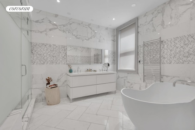 bathroom with a freestanding bath, double vanity, recessed lighting, a stall shower, and tile walls