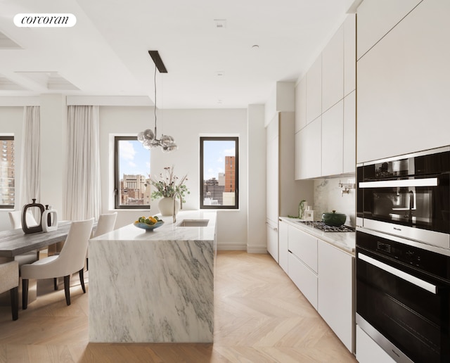 kitchen featuring a center island with sink, appliances with stainless steel finishes, light parquet flooring, pendant lighting, and white cabinets