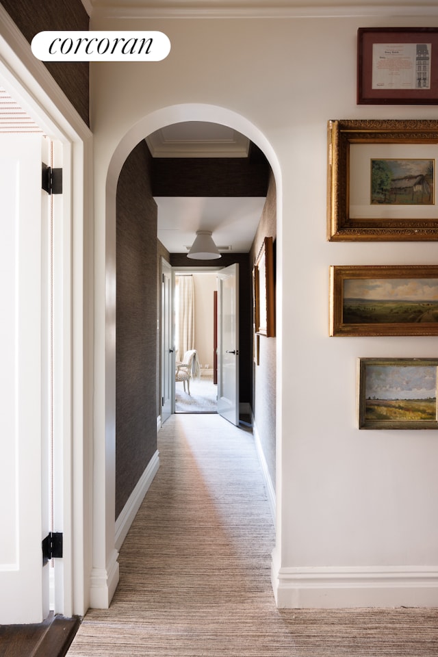 hallway featuring baseboards, arched walkways, crown molding, and carpet flooring