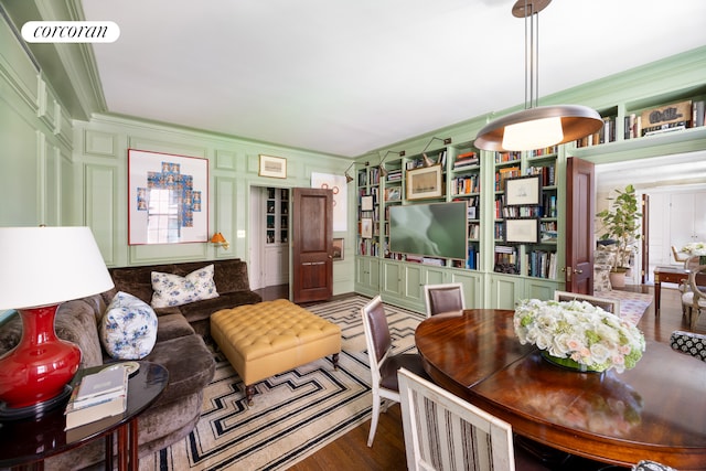 living room featuring visible vents, ornamental molding, a decorative wall, and wood finished floors