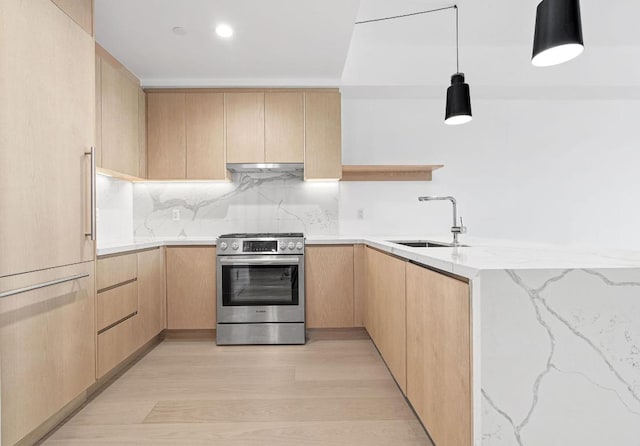 kitchen with light stone counters, a sink, stainless steel range with gas cooktop, light brown cabinetry, and decorative light fixtures