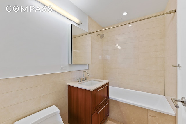 full bathroom with tile walls, toilet, tiled shower / bath, and vanity