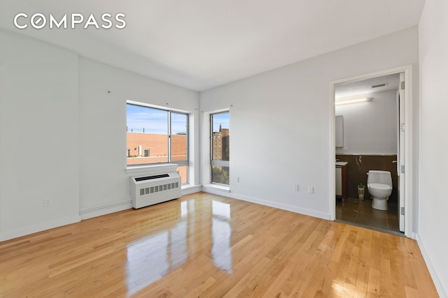 unfurnished bedroom with hardwood / wood-style flooring, radiator heating unit, baseboards, and connected bathroom