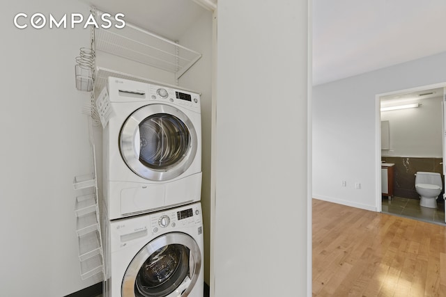 washroom featuring stacked washer / dryer, light wood finished floors, and baseboards