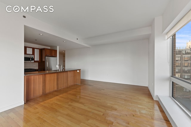 kitchen with light wood finished floors, dark countertops, backsplash, appliances with stainless steel finishes, and a peninsula