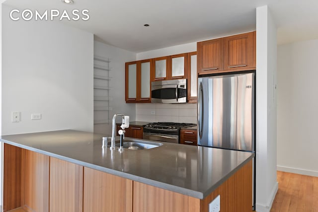 kitchen with appliances with stainless steel finishes, a sink, a peninsula, dark countertops, and glass insert cabinets