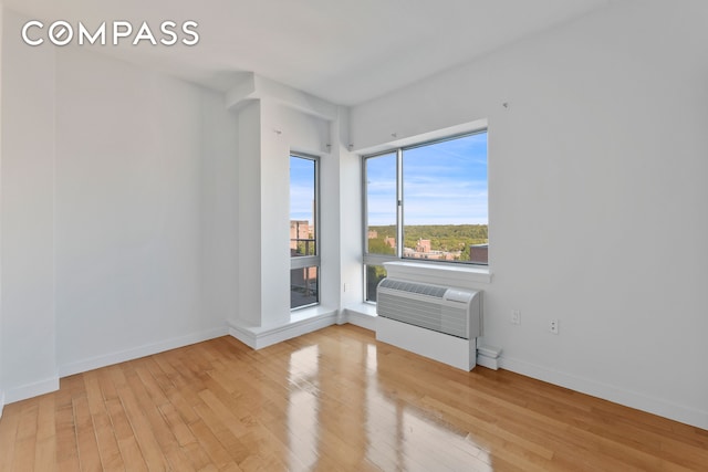 unfurnished room with baseboards, a wall mounted air conditioner, and light wood-style floors