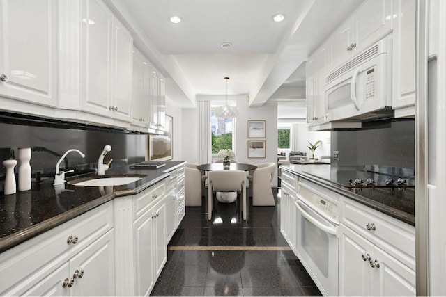 kitchen with sink, hanging light fixtures, white appliances, dark stone counters, and white cabinets