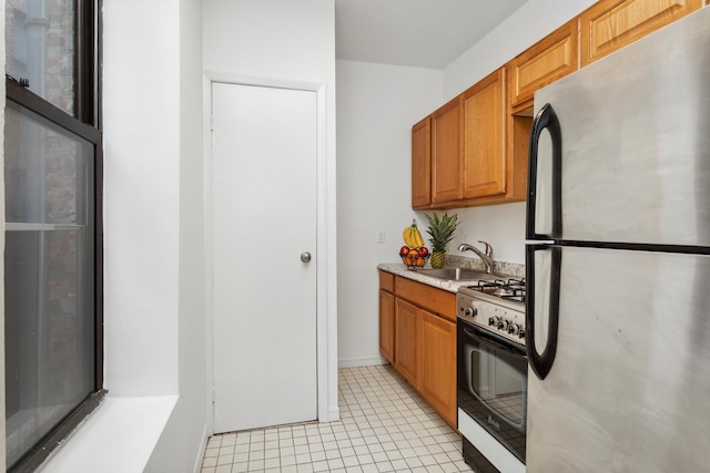 kitchen featuring light tile patterned floors, freestanding refrigerator, a sink, light countertops, and gas range oven