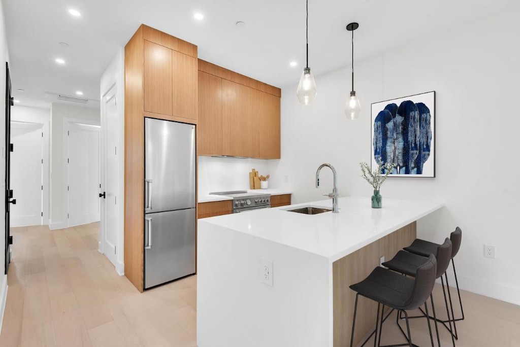 kitchen featuring sink, appliances with stainless steel finishes, hanging light fixtures, a kitchen bar, and kitchen peninsula