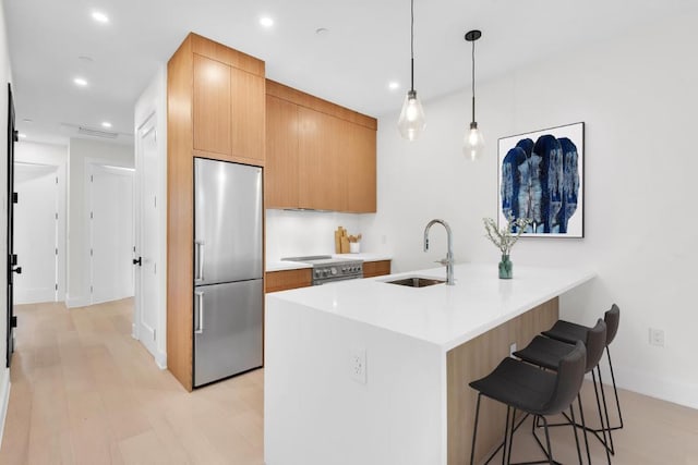 kitchen featuring sink, appliances with stainless steel finishes, hanging light fixtures, a kitchen bar, and kitchen peninsula