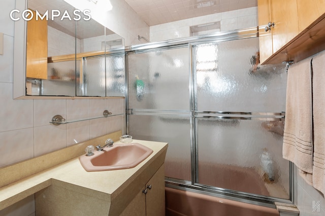 full bath with tasteful backsplash, tile walls, vanity, and bath / shower combo with glass door