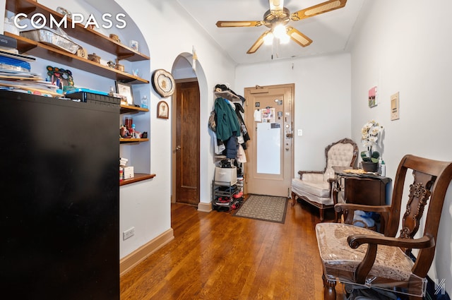 living area with a ceiling fan, arched walkways, baseboards, and wood finished floors