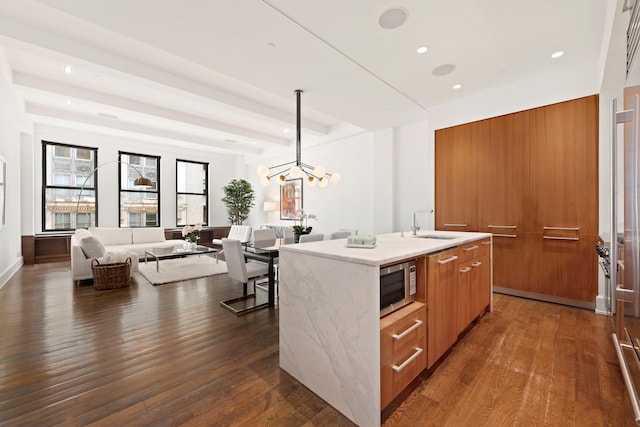 kitchen with modern cabinets, stainless steel microwave, brown cabinetry, a sink, and an island with sink