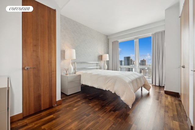 bedroom featuring an accent wall, baseboards, dark wood-type flooring, and a city view