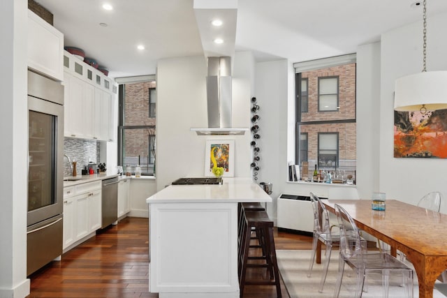 kitchen with a breakfast bar, backsplash, appliances with stainless steel finishes, dark wood-type flooring, and wall chimney range hood