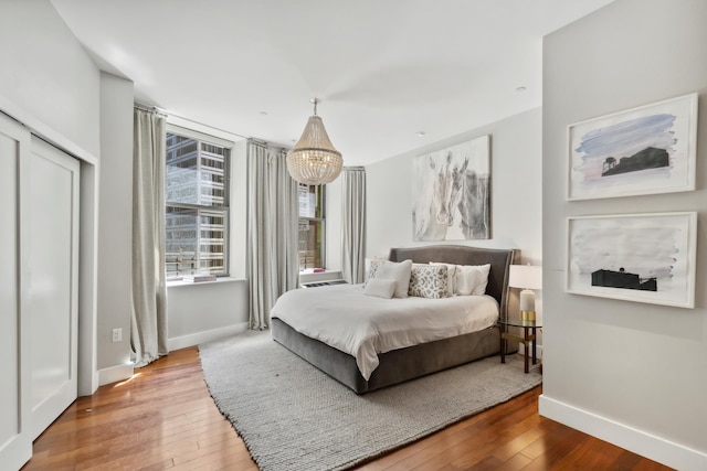 bedroom with an inviting chandelier, wood-type flooring, and baseboards