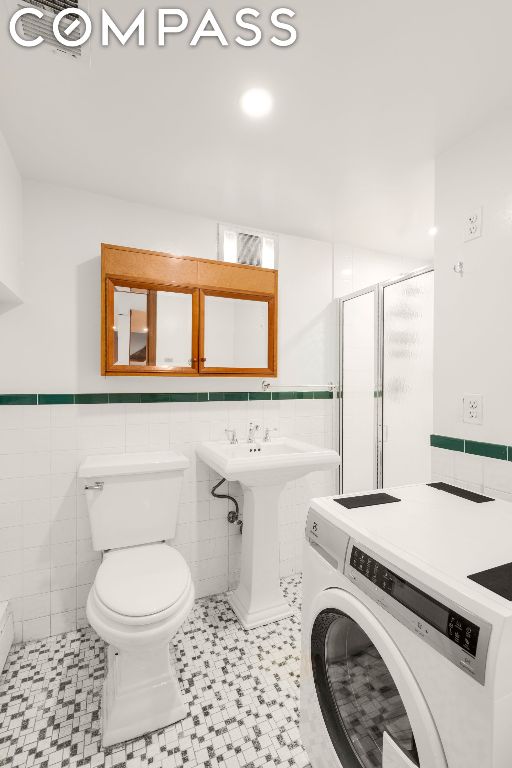 bathroom featuring tile walls, walk in shower, washer / dryer, and toilet