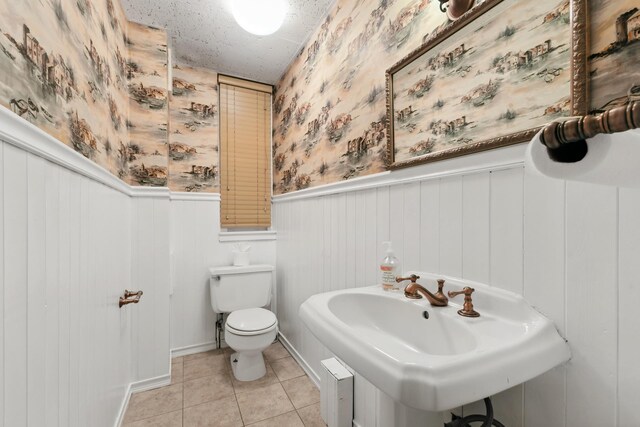 45 E 62nd St Unit 1B, New York City, NY 10065 - half bathroom with wallpapered walls, a wainscoted wall, toilet, tile patterned floors, and a sink