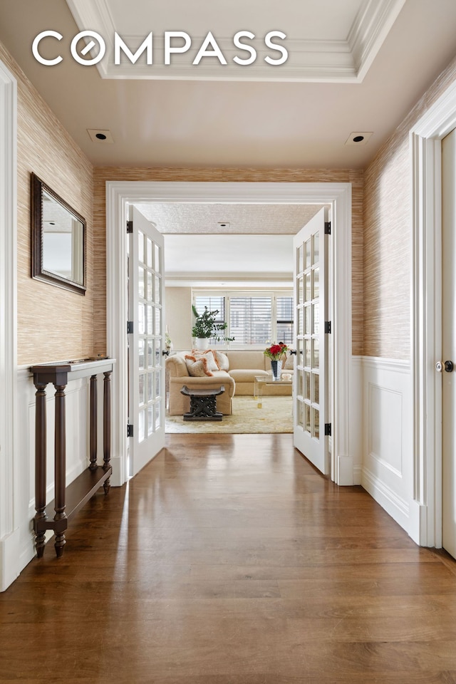 hallway with wainscoting, wood finished floors, a tray ceiling, crown molding, and french doors