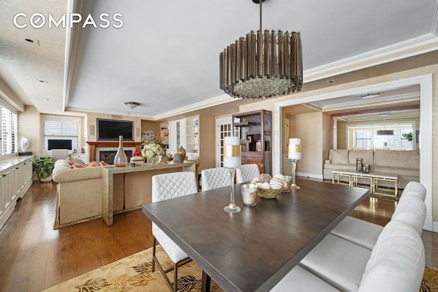 dining space featuring ornamental molding, wood finished floors, and a glass covered fireplace