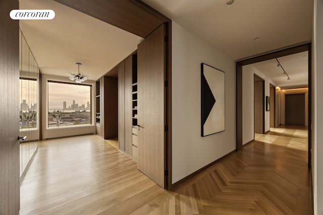 corridor with track lighting, visible vents, parquet flooring, a city view, and a notable chandelier