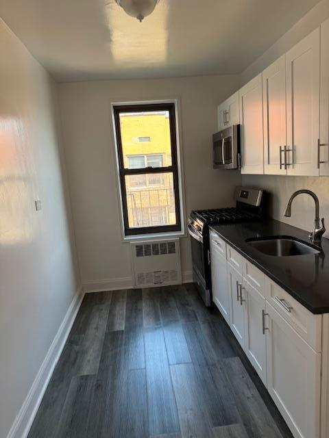 kitchen with radiator, sink, stainless steel appliances, and white cabinetry