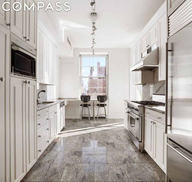 kitchen with tasteful backsplash, hanging light fixtures, high quality appliances, white cabinets, and sink