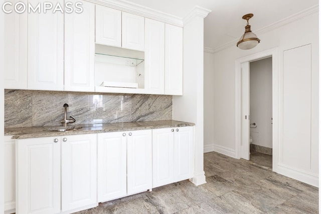 kitchen featuring white cabinetry, backsplash, stone counters, crown molding, and sink