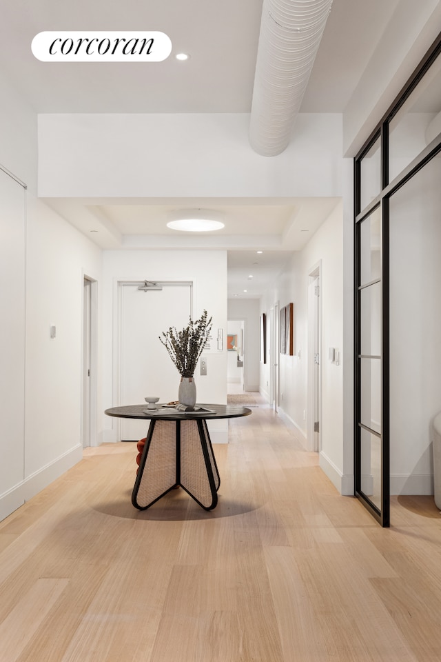 hallway featuring baseboards, a raised ceiling, and recessed lighting