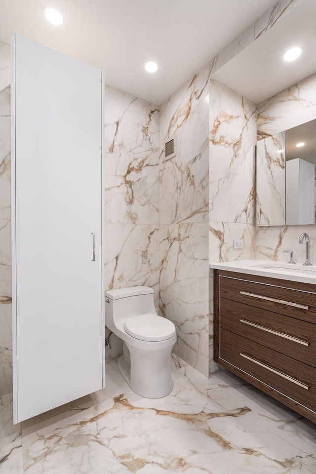 bathroom with visible vents, toilet, stone wall, and vanity