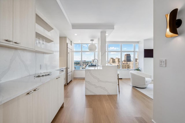 kitchen featuring sink, light wood-type flooring, an island with sink, light stone countertops, and backsplash