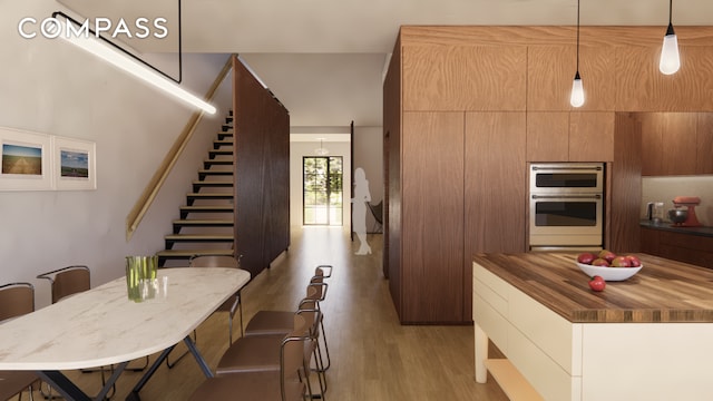 kitchen with stainless steel double oven, light wood-type flooring, wooden counters, and pendant lighting