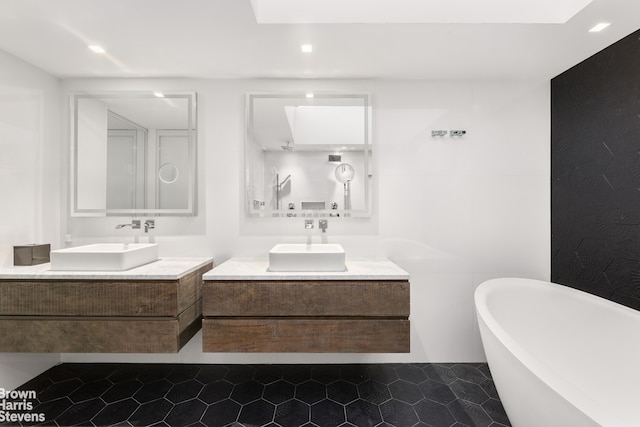 bathroom featuring two vanities, a soaking tub, and a sink