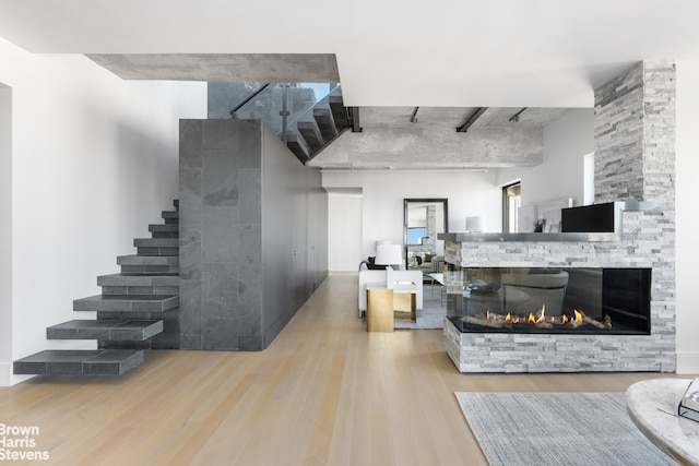 living area featuring stairs, a stone fireplace, a high ceiling, and light wood-style floors