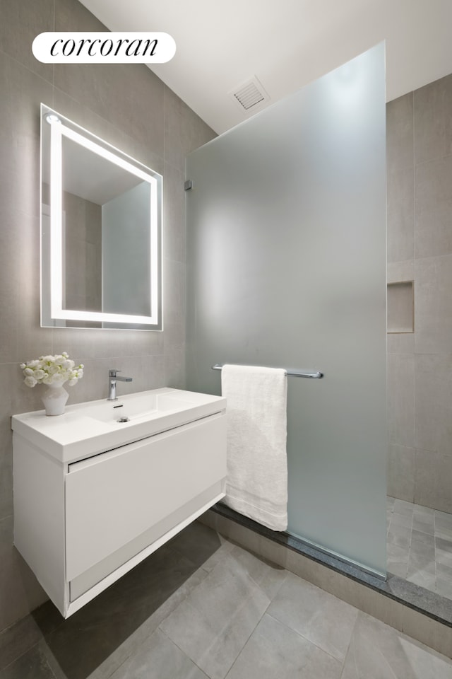 bathroom with vanity, visible vents, a tile shower, tile walls, and tile patterned floors