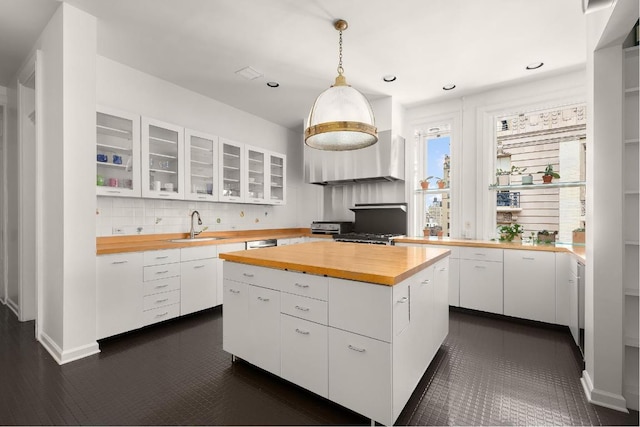 kitchen featuring butcher block counters, sink, a center island, pendant lighting, and white cabinets