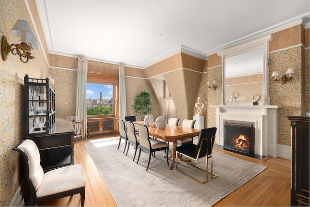 dining room featuring crown molding, wood-type flooring, a lit fireplace, and wallpapered walls