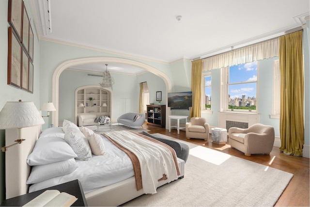 bedroom with arched walkways, ornamental molding, and wood finished floors