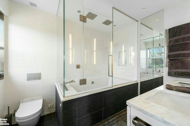 bathroom with visible vents, toilet, tiled shower / bath combo, vanity, and tile walls