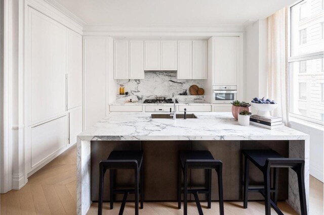 kitchen with white oven, white cabinetry, sink, and a kitchen breakfast bar